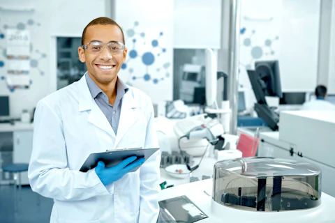 Chemistry is his passion. Handsome young African male scientist wearing protective glasses smiling happily holding his clipboard working at the lab professionalism occupation job people copyspace